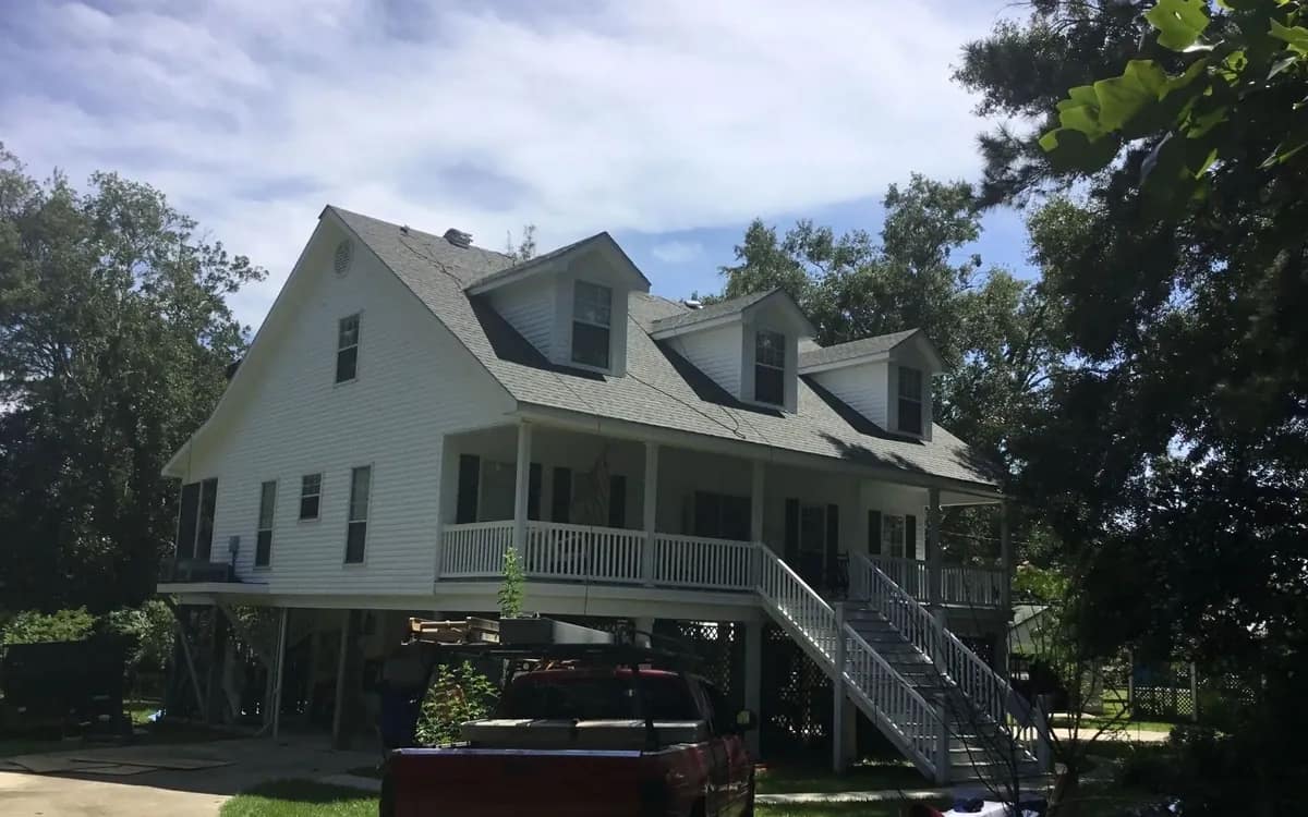 Elevated coastal home with a freshly installed light-gray shingle roof, Liberty Roofing truck in the driveway