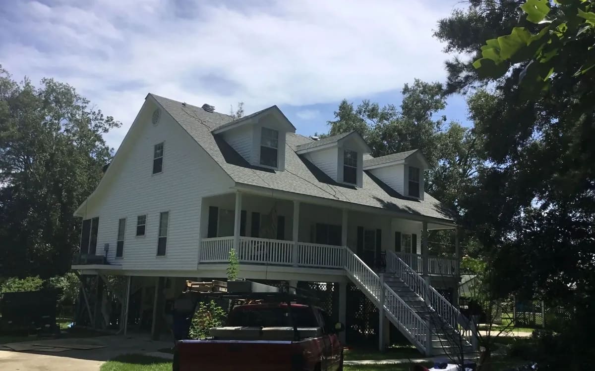 Elevated coastal home with a freshly installed light-gray shingle roof, Liberty Roofing truck in the driveway