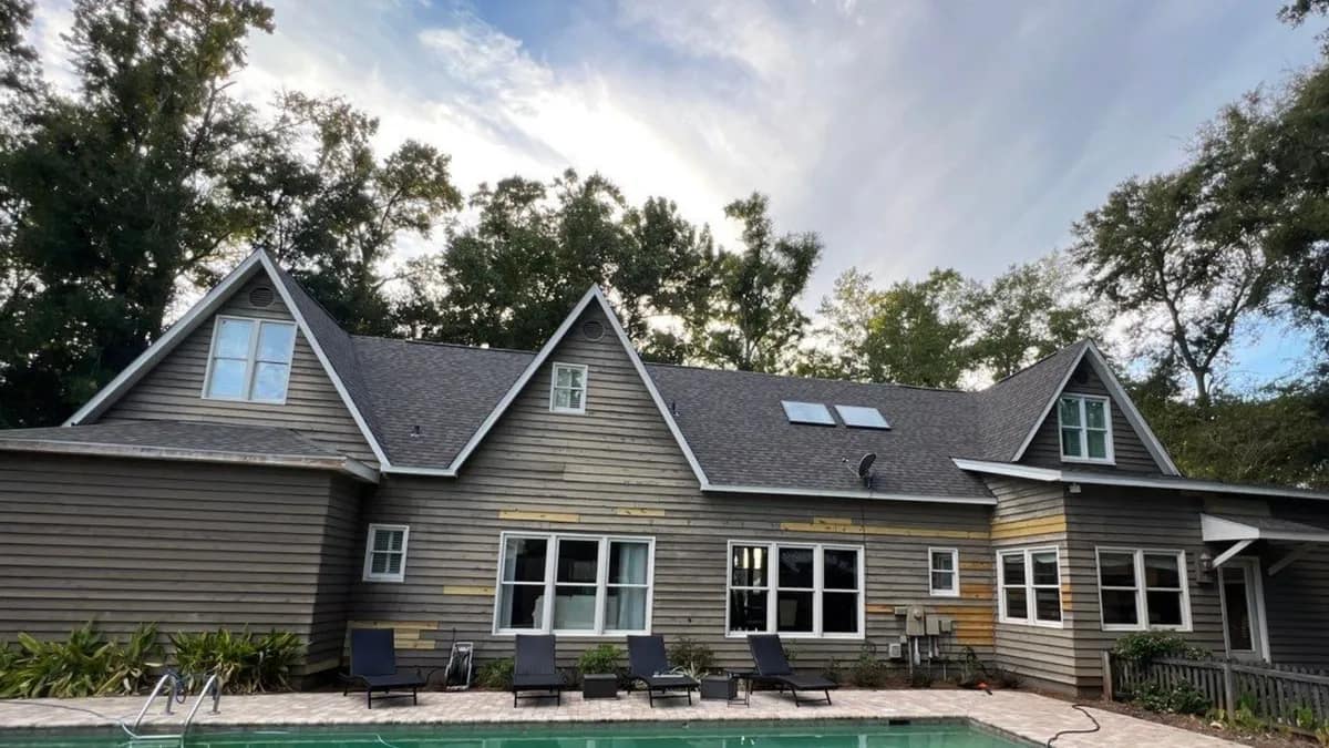 Large gray Baldwin County home under a finished dark architectural shingle roof, pool in the foreground