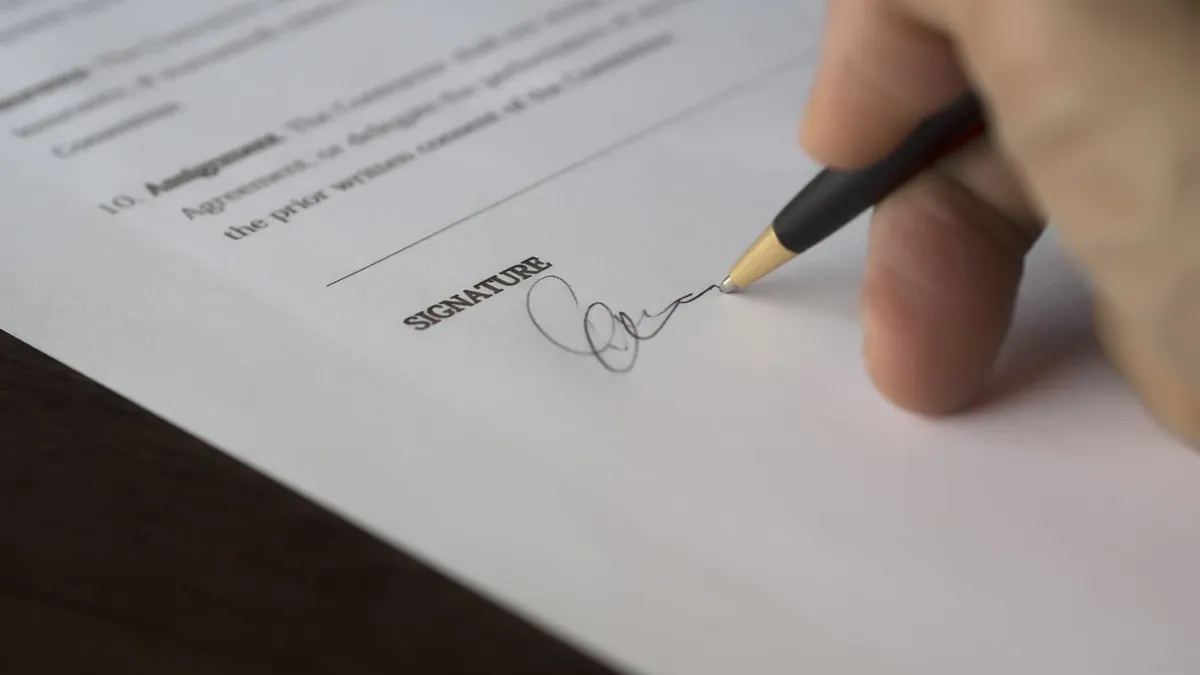 A hand signing the signature line directly beneath a contract's assignment clause