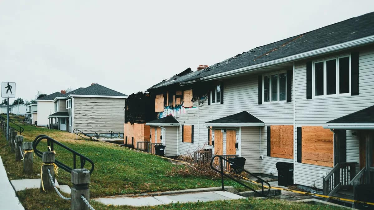 Plywood-boarded windows and torn-open roofing on a row of storm-damaged townhomes