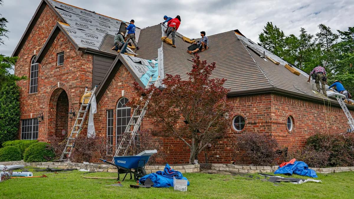 A brick home mid-reroof, underlayment down over the exposed deck and ladders set against the eave