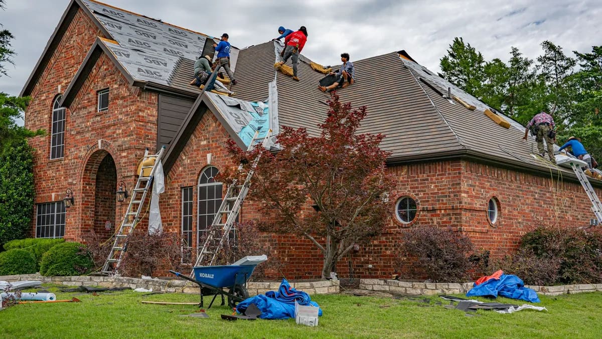 A brick home mid-reroof, underlayment down over the exposed deck and ladders set against the eave