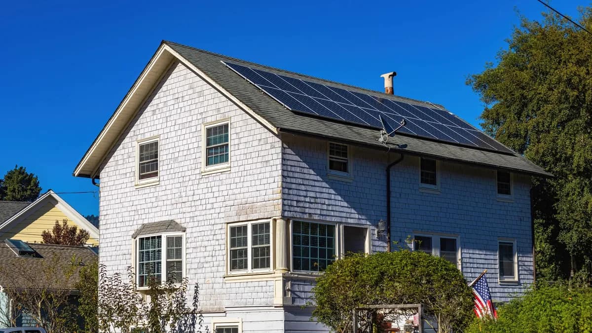 Solar panels mounted on the asphalt shingle roof of a two-story shingle-sided house
