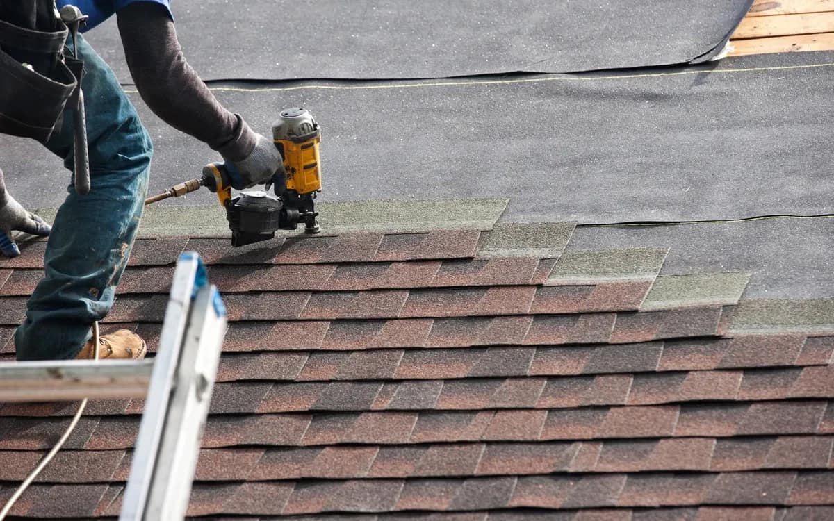 Liberty Roofing crew member nailing new shingle courses over exposed underlayment mid-job