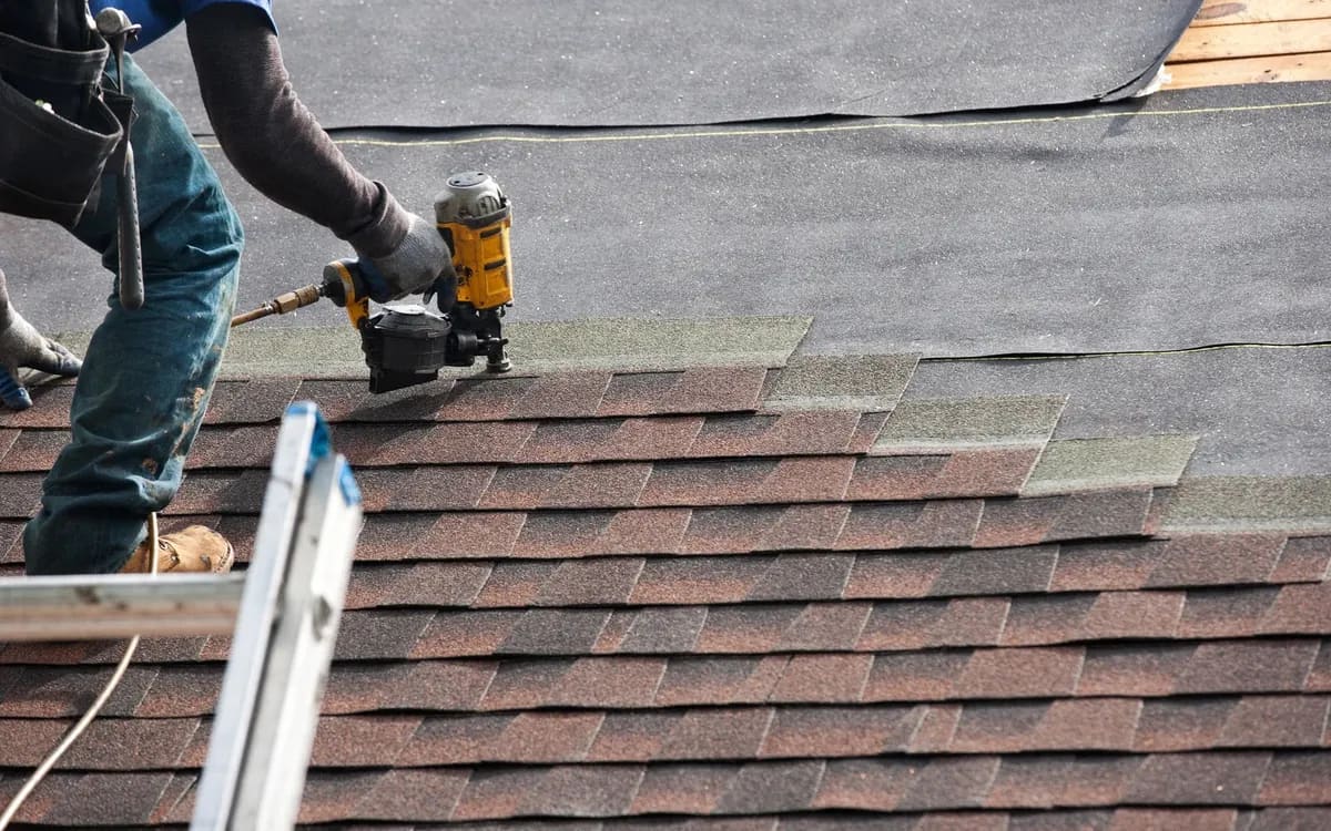 Liberty Roofing crew member nailing new shingle courses over exposed underlayment mid-job