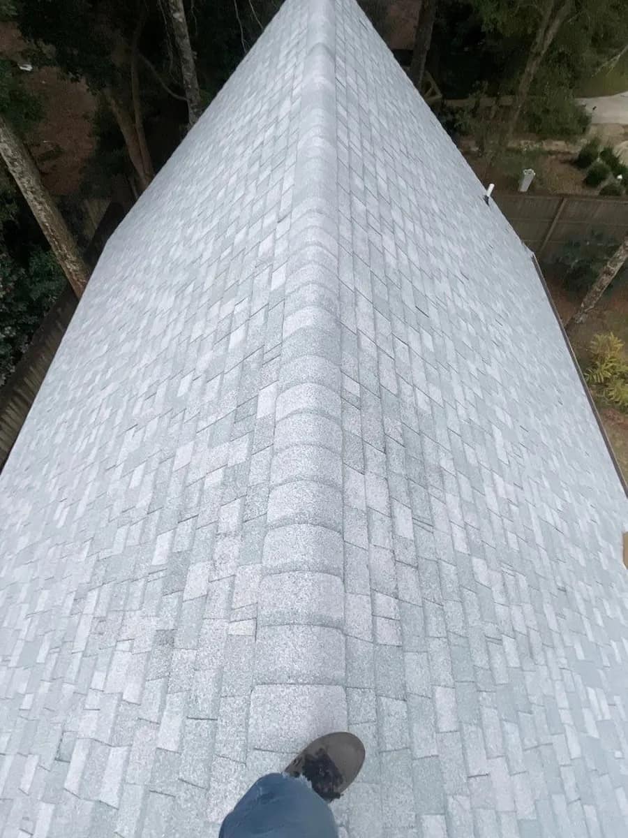 Looking down the ridge of a finished light-gray shingle roof from a roofer's own vantage point