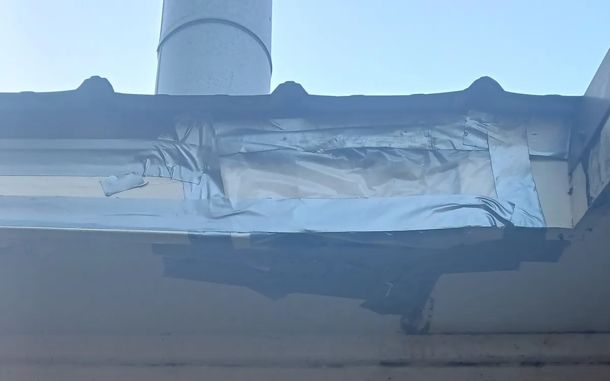 Temporary tape patch sealing storm-damaged soffit and fascia under a roof eave