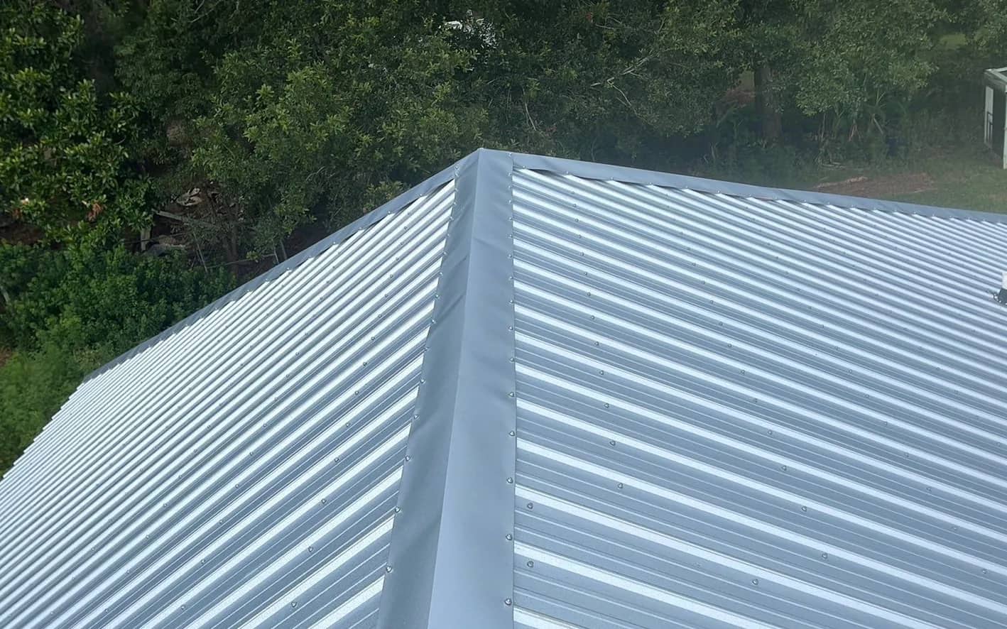 Close view of a newly installed corrugated metal roof meeting at the hip, over a wooded Baldwin County property.