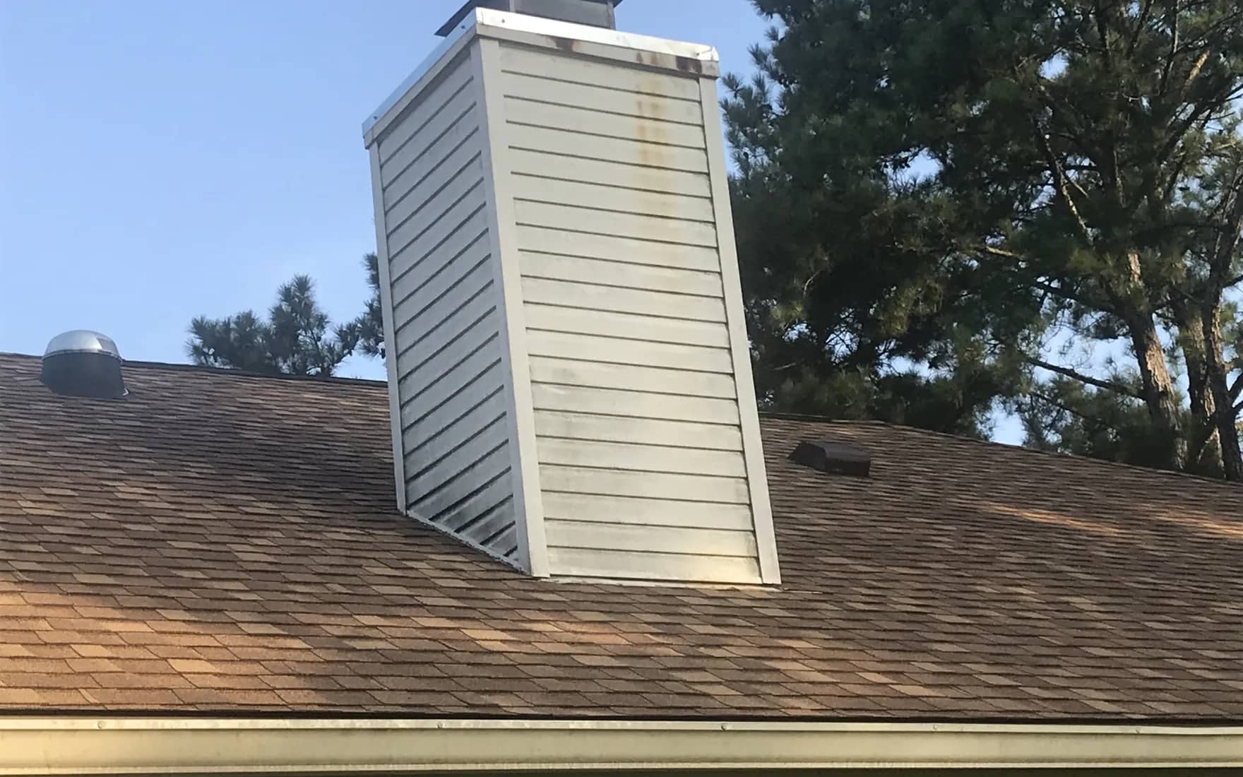 Chimney chase and new metal cap flashing on a shingle roof, photographed close on a Gulf Coast job.