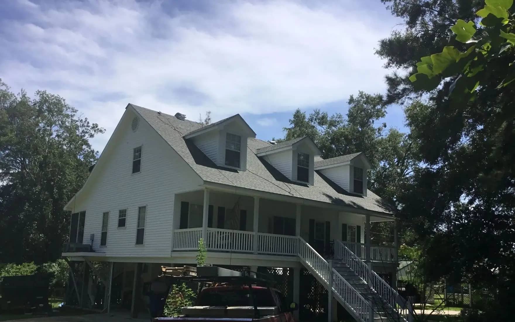 White elevated coastal home with a freshly installed light-gray roof under a clear sky.